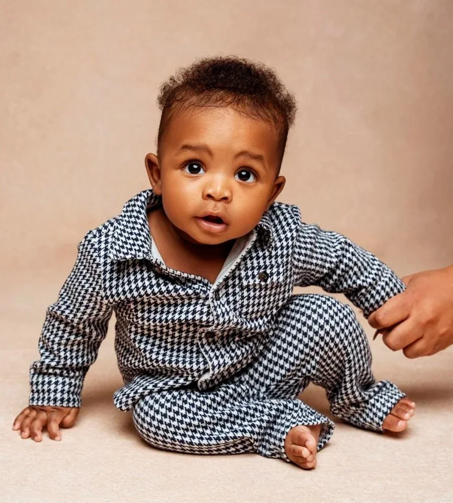 Adorable baby boy in a black-and-white houndstooth suit sitting for a milestone photography session in a studio.