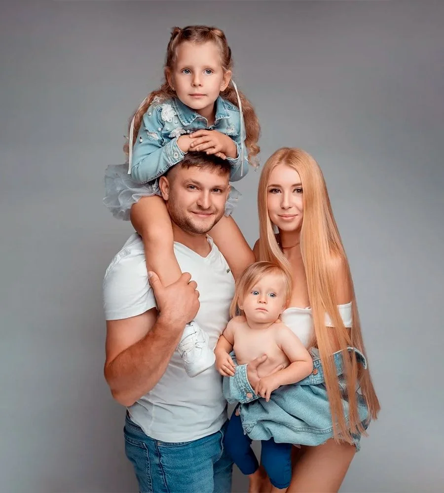 Beautiful studio family portrait of parents with their two young daughters wearing matching denim outfits against a plain gray backdrop.